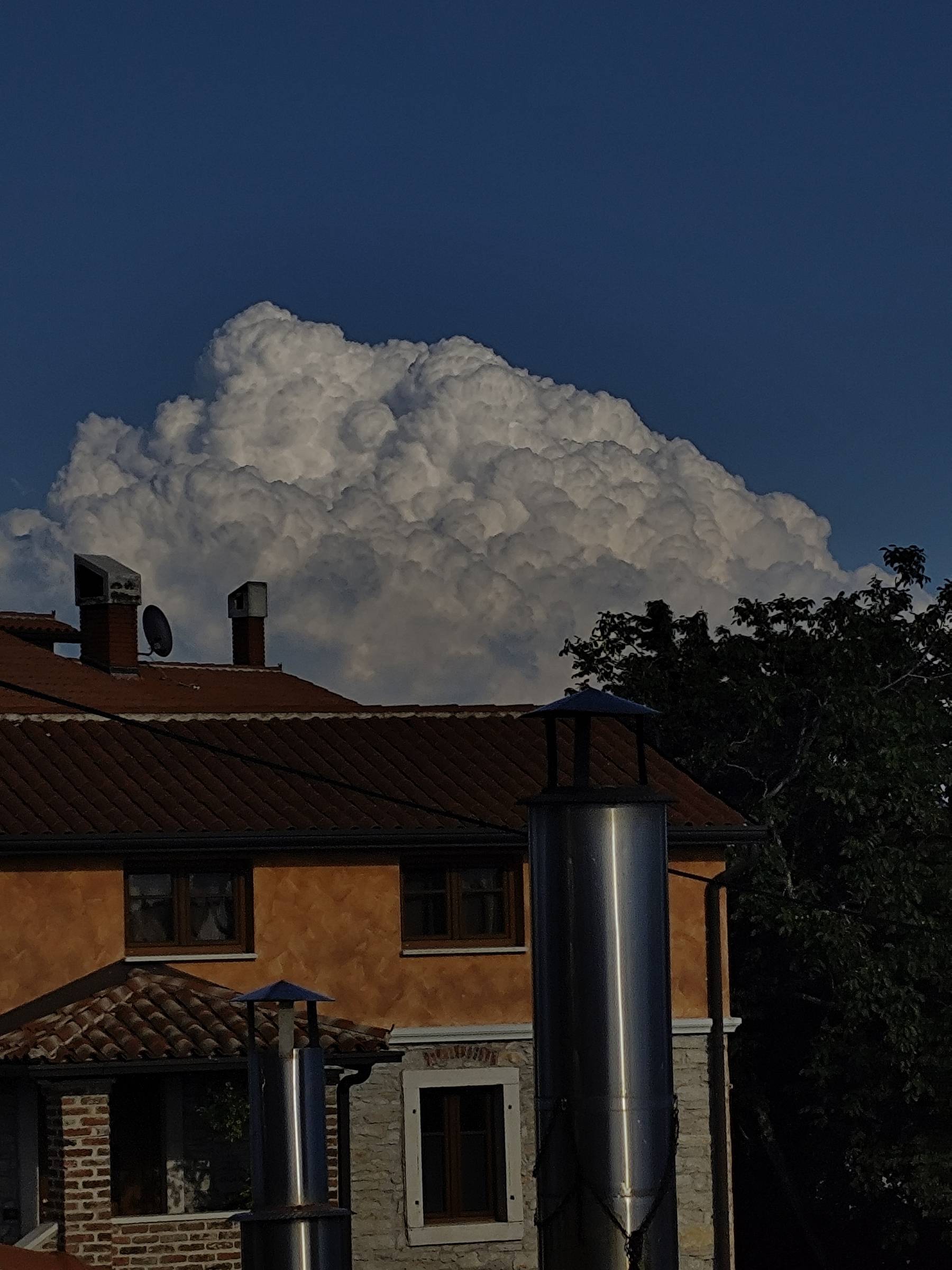 Velik kumulonimbus za strehami istrskih hiš v poznem popoldanskem soncu.