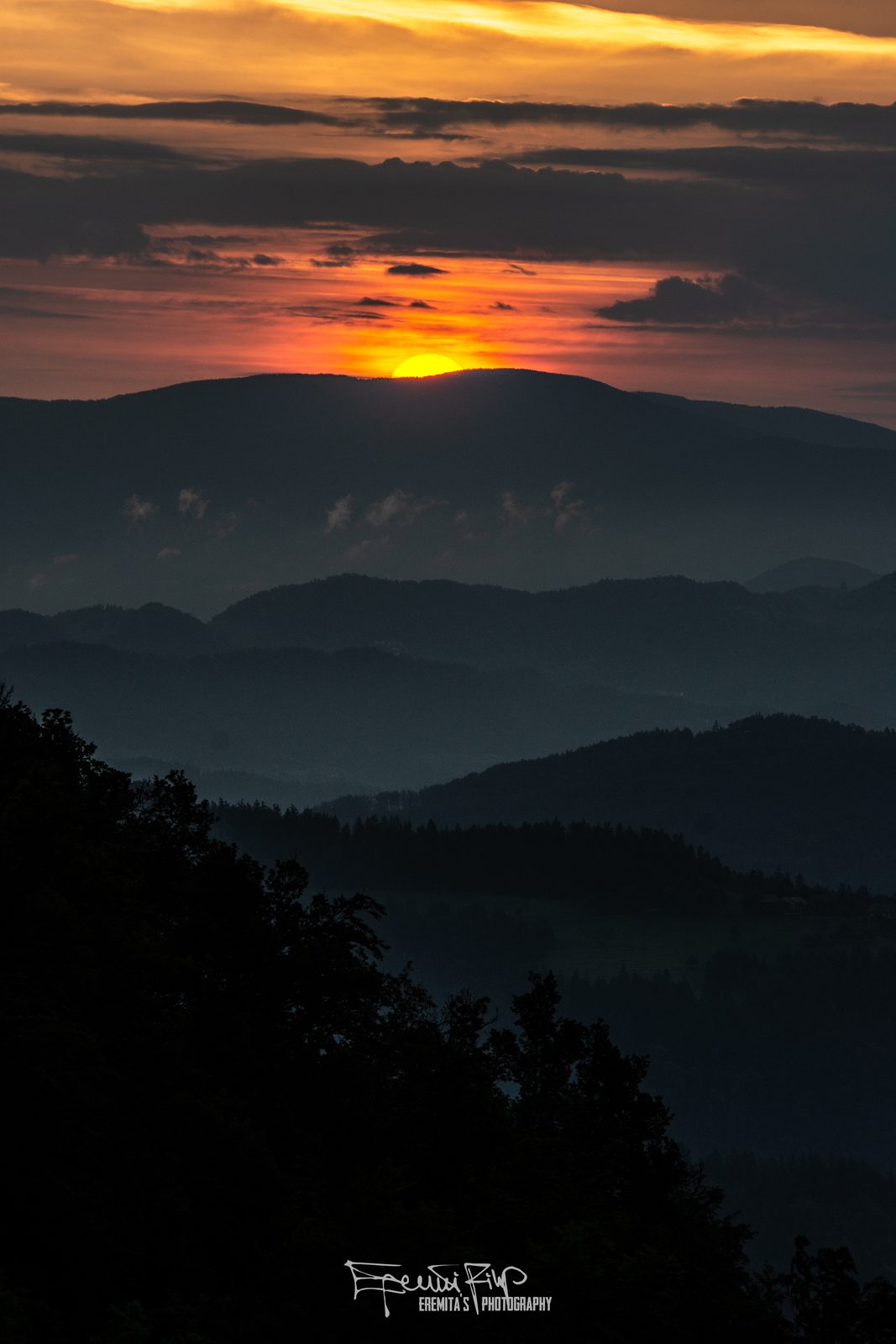 Ognjeno rdeč sončni zahod nad plastmi hribov v Zgornji Savinjski dolini, vročina še vedno v zraku.